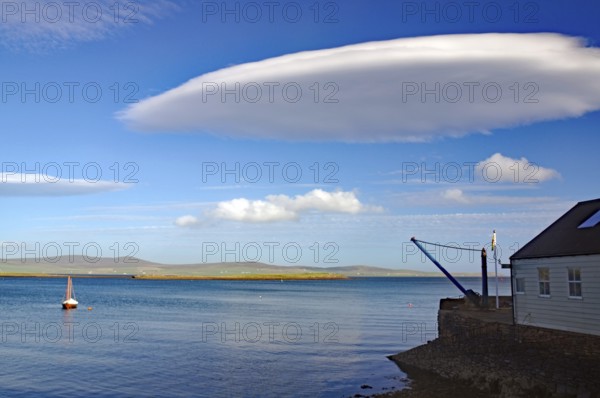 A tranquil ocean view with unique cloud formation and sailboat, UFO clouds, Stromness, Orkney Islands, Scotland, United Kingdom