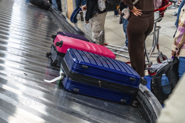 Colorful suitcases resting on an airport baggage claim carousel, while passengers eagerly waiting to collect their luggage after arriving at their travel destination
