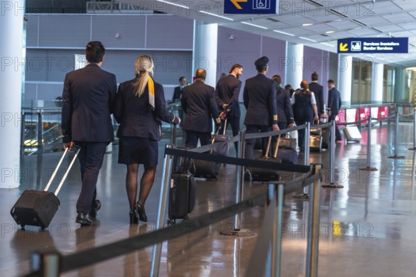 Pilots and flight attendants are walking through a modern airport terminal, pulling rolling suitcases behind them, preparing for their next flight
