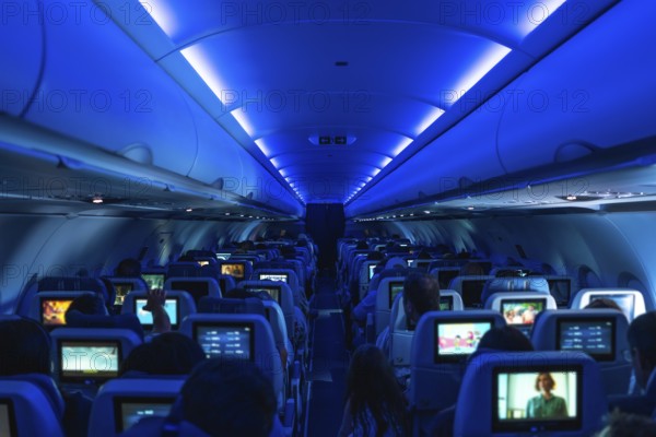 Passengers enjoying in flight entertainment while watching movies on personal screens, surrounded by a cozy atmosphere under blue ambient lighting in the aircraft cabin