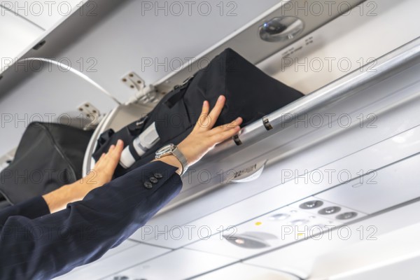 Businessman wearing suit and watch is storing hand luggage in the overhead compartment of a commercial airplane during a flight, ensuring safe and convenient storage during air travel