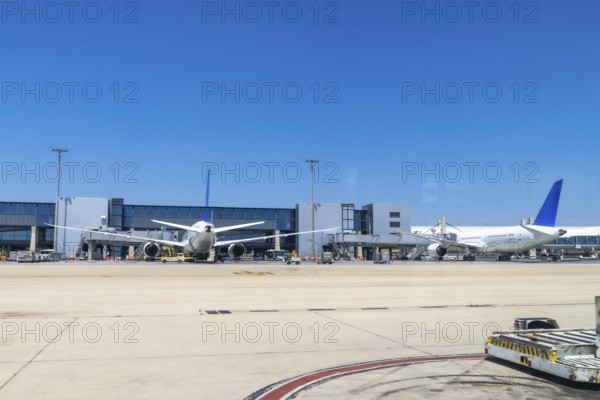 Two large passenger airplanes parked at airport gates under a bright sunny sky, waiting for passengers and preparing for their upcoming departures on a bustling day of travel