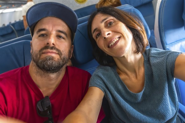 Happy couple taking a selfie on an airplane, enjoying their flight while capturing joyful moments together. Smiling and sharing their adventure high above the ground