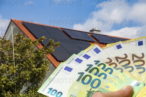 (Photo montage) Man holding euro banknotes in front of a solar roof
