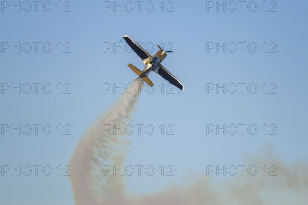 Golden stunt aerobatic plane performing stunts in blue sky with smoke trail. Concept of speed, difficulty, precision, risk
