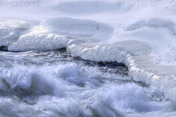 Ice formation formed by frost and freezing cold temperatures over running water of stream along riverbank / river bank in winter