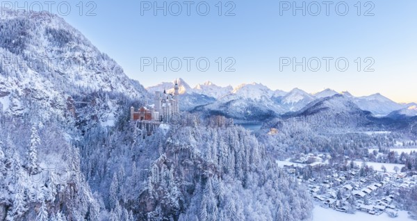 Neuschwanstein Castle is perched in the snowy alpine landscape, surrounded by peaceful forests under blue skies, Schwangau near Füssen, Ostallgäu, Allgäu, Bavaria, Germany