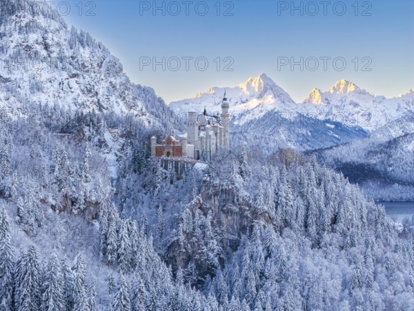 Neuschwanstein Castle surrounded by mountains in snow, in the warm light of sunrise, Schwangau near Füssen, Ostallgäu, Allgäu, Bavaria, Germany