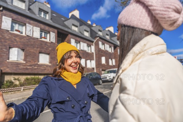 Two cheerful women friends dressed in winter clothes meeting and greeting each other with open arms on a city street, expressing happiness and connection