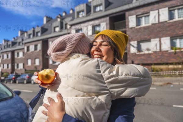 Happy mother and child sharing an affectionate hug while standing on a city street, enjoying a sunny day together, with the child holding a half eaten apple