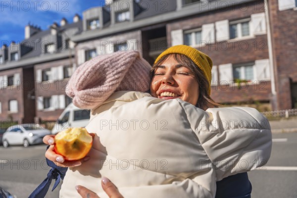 Happy young mother with closed eyes embraces her child on a sunny city street, smiling while holding a bitten apple candid moment of warm family bonding and joy