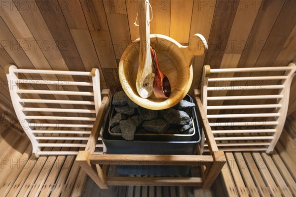 Steam and hot stone wooden cedar compact sauna interior with heating stone electrical device, hot water bucket and benches