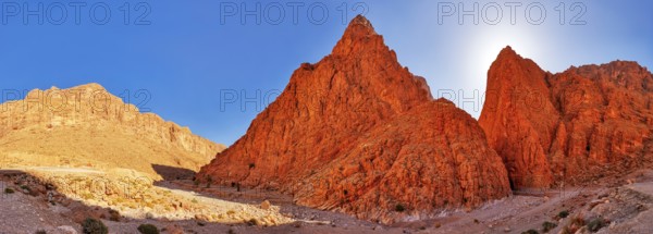 Panoramic view of bright red rocks in desert landscape under clear sky, Todra Gorge in Morocco