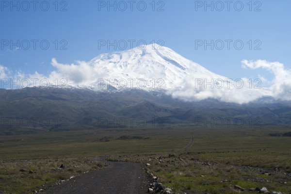 A snow-covered mountain rises majestically under a clear blue sky with scattered clouds, near Cevirme, Great Ararat, Büyük Agri Dagi, Dogubayazit, Dogubayazit, Dogubeyazit, Agri Province, East Anatolia, Turkey