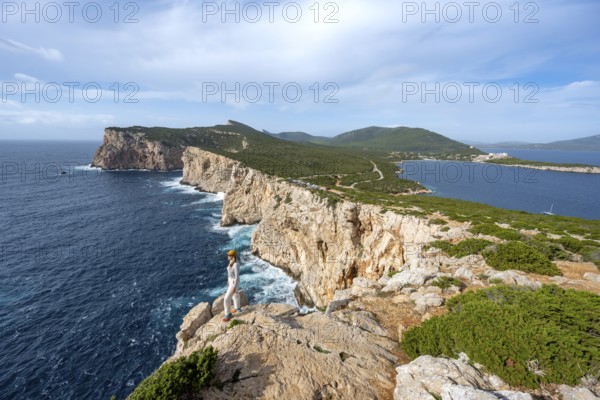 Tourist enjoying the view of steep cliffs by the sea, coastal landscape, cliffs on the Capo Caccia headland, Alghero, Sardinia, Italy