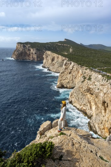 Tourist enjoying the view of steep cliffs by the sea, coastal landscape, cliffs on the Capo Caccia headland, Alghero, Sardinia, Italy