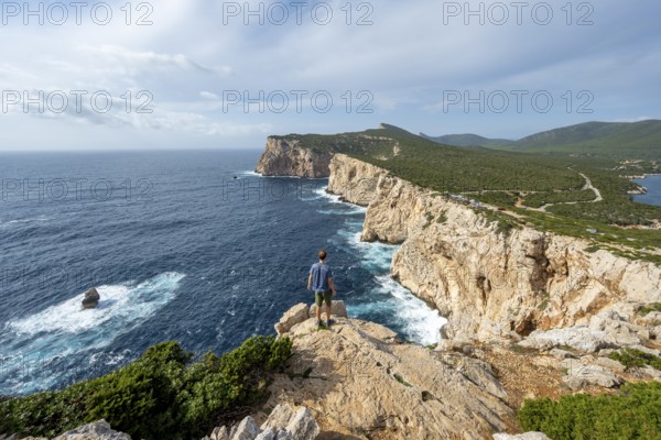 Tourist enjoying the view of steep cliffs by the sea, coastal landscape, cliffs on the Capo Caccia headland, Alghero, Sardinia, Italy