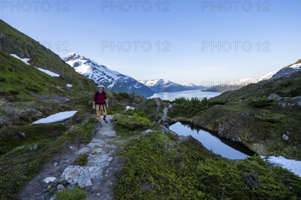 Hikers on Portage Pass, snow-covered mountains and Fjord Passage Canal, near Whittier, Alaska, USA