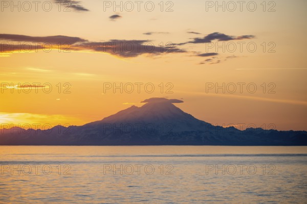 View of Cook Inlet on white mountain peaks of Mount Redoubt at sunset, picturesque golden light of the midnight sun, mountains of the Aleutian Range, Anchor Point, Anchor River State Recreation Area, Alaska, USA