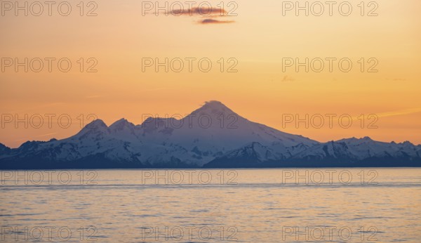 View of Cook Inlet on white mountain peaks of Mount Iliamna at sunset, picturesque golden light of the midnight sun, mountains of the Aleutian Range, Anchor Point, Anchor River State Recreation Area, Alaska, USA