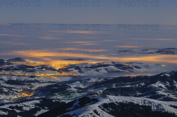 Night shot, long exposure of the 2506 meter high Säntis into the wintery, snow-covered, fog-covered foothills of the Alps illuminated by the villages, during a clear full moon night, Canton of Appenzell, Switzerland