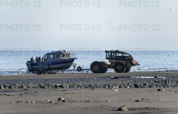 Motor boat on a boat trailer is driven into water by a tractor on a beach, Anchor Point, Alaska, USA