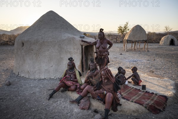 Married Himba woman with their babies in their arms sitting in front of the first woman's hut, in the morning, traditional Himba village, Kaokoveld, Kunene, Namibia