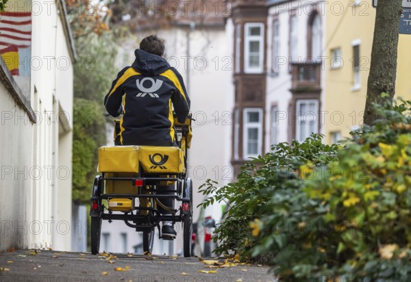Deutsche Post mailmen on a bicycle through the city. Stuttgart, Baden-Württemberg, Germany