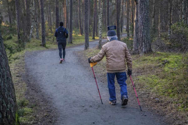 Exercisers on a forest path, a younger man running and an older man walking with poles in Ystad, Skåne County, Sweden, Scandinavia