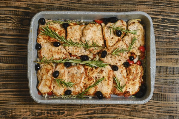 Roasted pork chops placed over a bed of colourful vegetables, garnished with olives and fresh herbs