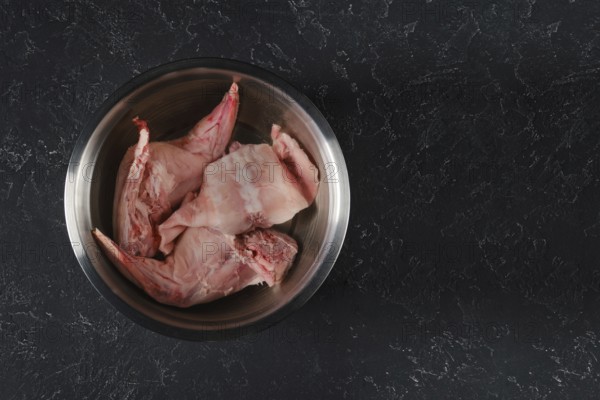 Fresh rabbit hind legs and a saddle are soaked in water with vinegar in a metal bowl. The process of softening raw meat and reducing the taste of wild rabbit