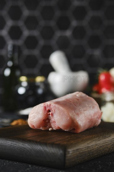 Close-up view of a piece of raw rabbit meat on a wooden cutting board in a contemporary kitchen. Surrounding ingredients include herbs, spices, and kitchen tools, highlighting the preparation for cooking