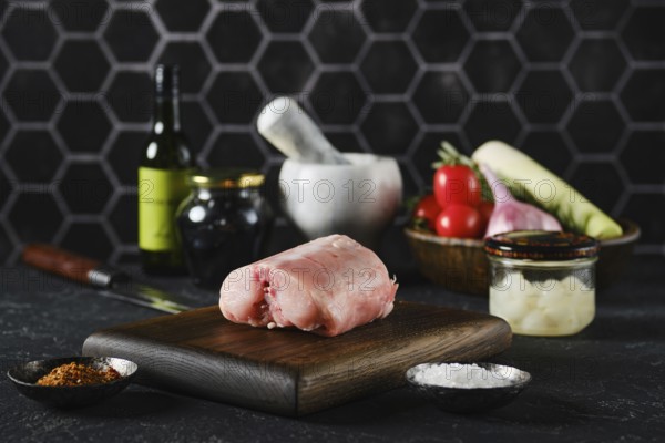 A fresh rabbit saddle on a wooden cutting board surrounded by fresh vegetables and cooking tools