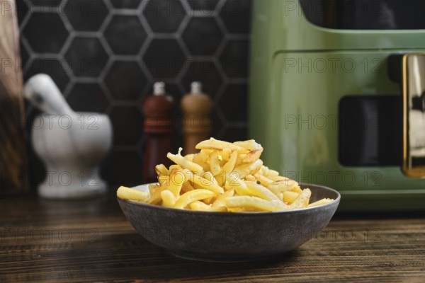 Fries are piled high in a dark bowl on a kitchen counter. The setting features a stylish air fryer and decor that blends modern design with rustic elements, creating a cozy atmosphere