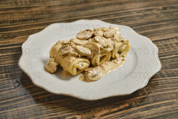 Tasty crepes filled with savory meat and topped with a creamy mushroom sauce, served on a decorative white plate