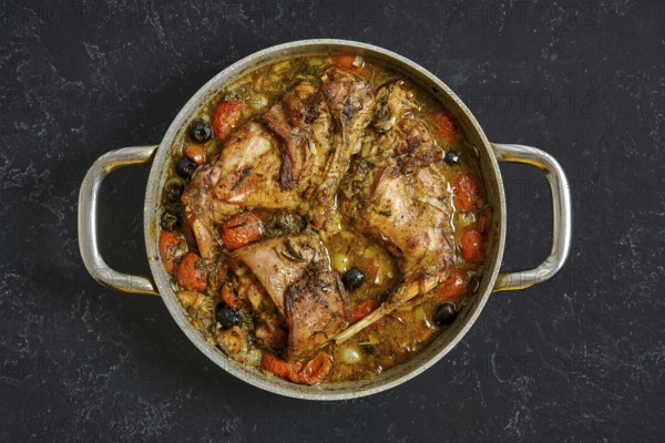 A delicious rabbit hind leg stew simmers in a large pot, featuring juicy meat surrounded by carrots, olives, and other vegetables in a rich sauce. Ideal for a cozy dinner or family meal
