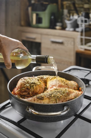 Close-up view of hand pouring dry white wine in a pot with rabbit hind legs and saddle
