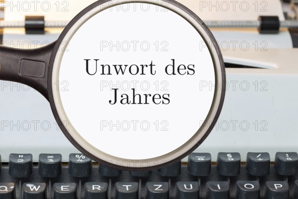 (Photo montage) Magnifying glass shows the text UNWORD OF THE YEAR in front of a typewriter