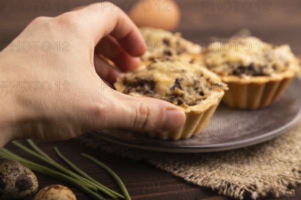 Tartlets with meat and cheese with hand on brown wooden background and linen textile. side view, close up, selective focus