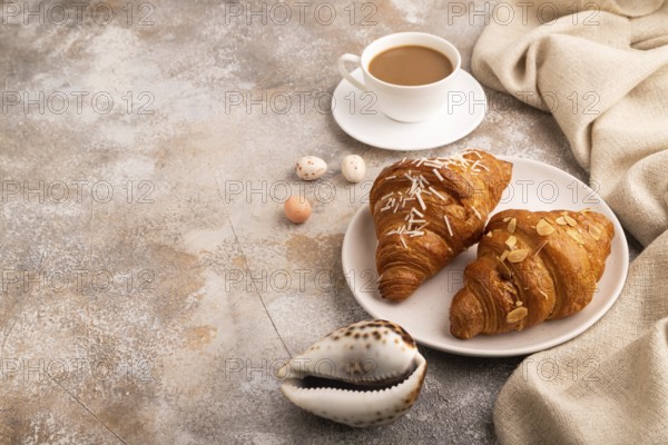 Croissant on white plate on brown concrete background and linen textile, cup of coffee, side view, copy space