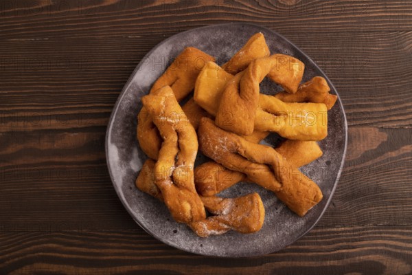 Crunchy biscuit Brushwood cookies sprinkled with powdered sugar on brown wooden background, top view, flat lay, close up