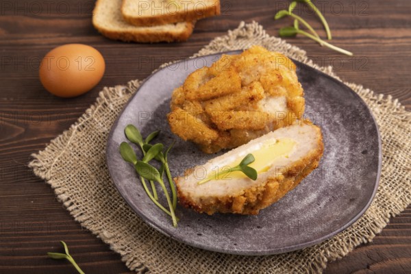 Chicken Schnitzel on gray plate with microgreen on brown wooden background and linen textile. side view, close up