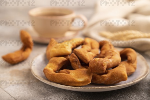 Crunchy biscuit Brushwood cookies sprinkled with powdered sugar on brown concrete background and linen textile, cup of coffee, side view, selective focus