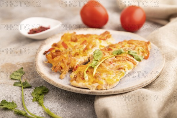 Baked chicken meat with cheese and tomatoes on brown concrete background and linen textile. side view, close up, selective focus