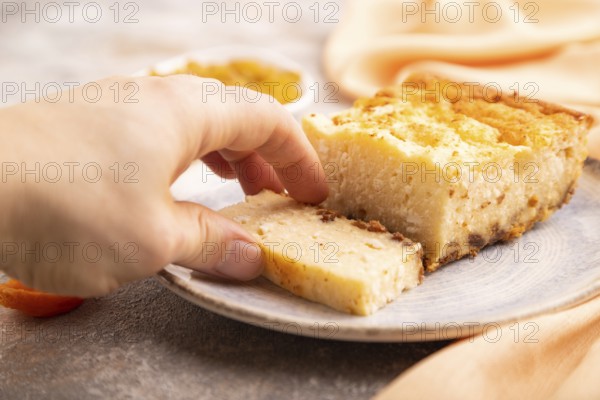 ?ottage cheese ?asserole, Curd cake, with dried apricots and raisins with hand on brown concrete background and orange textile, side view, selective focus, minimalism