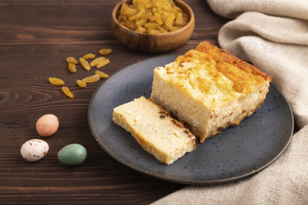 ?ottage cheese ?asserole, Curd cake, with dried apricots and raisins on brown wooden background and linen textile, side view, close up, minimalism