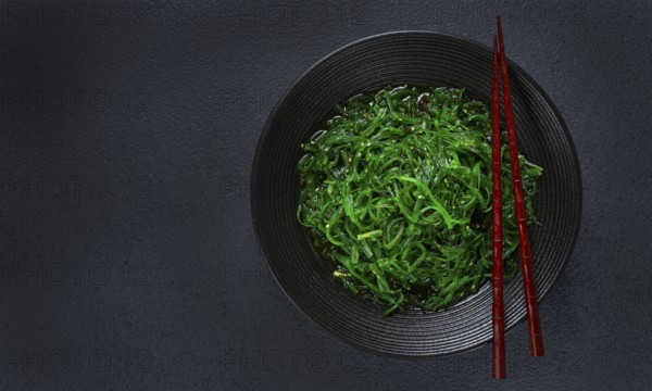 Chuka salad, made from fresh seaweed, with sesame dressing, served in a black bowl, with chopsticks