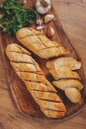 Garlic bread, baguette with garlic butter and herbs, on a wooden board, with herbs and garlic cloves