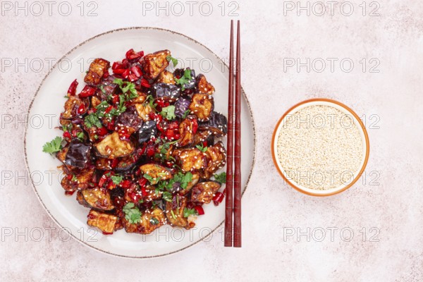 Fried eggplant, Chinese style, in sweet and sour sauce, with pepper and sesame seeds. on a white plate