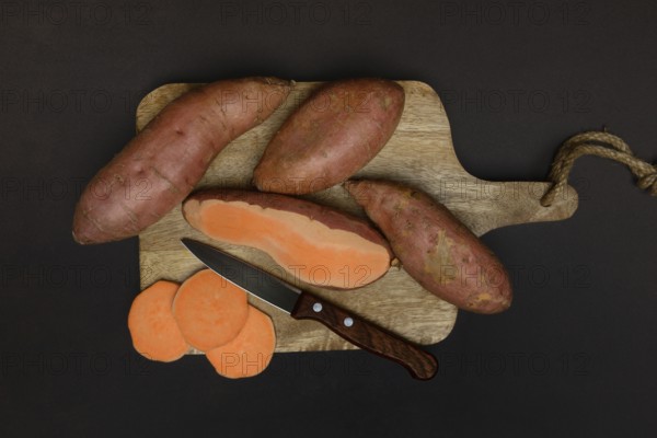 Sweet potatoes with kitchen knife on wooden board, Ipomoea batatas